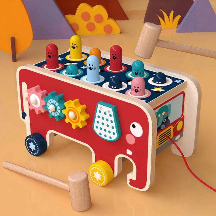 Colorful wooden toddler toy with gears, mallets, and pop-up animal pegs shaped like a bus
