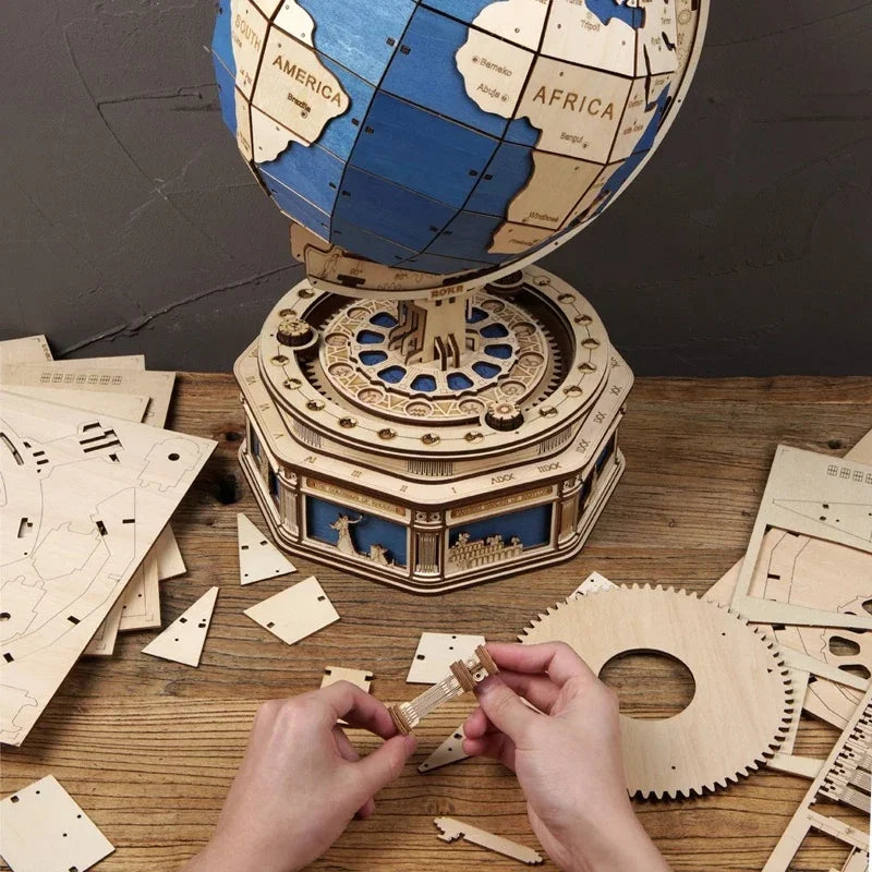 Hands assembling a wooden mechanical globe puzzle kit on a wooden table with laser-cut parts.