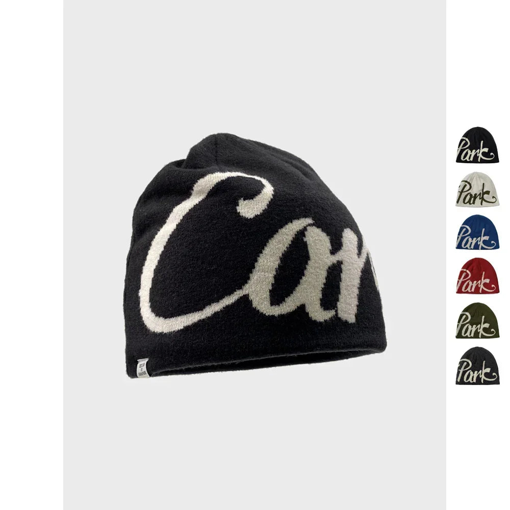 Black knitted beanie with bold white script, streetwear style, available in multiple colors.