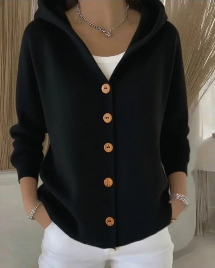 Woman wearing a black button-up hoodie with wooden buttons, white top and white pants