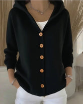 Woman wearing a black button-up hoodie with wooden buttons, white top and white pants