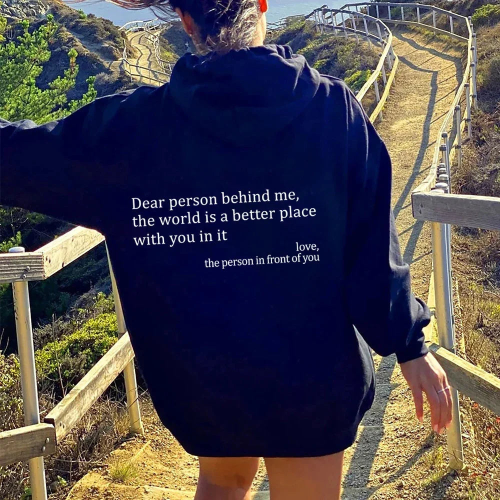 Woman outdoors in oversized black hoodie with positive quote, relaxed fit, walking on scenic trail