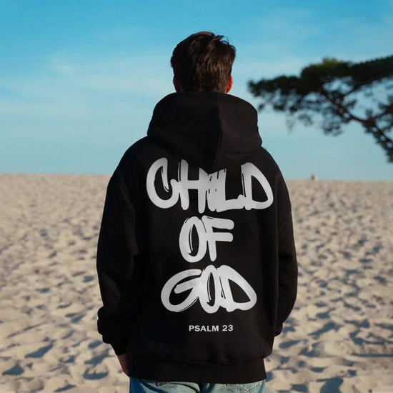 Man wearing black streetwear hoodie with bold white graffiti text, relaxed fit, on beach