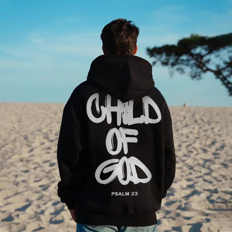 Black oversized streetwear hoodie with bold white graffiti text on beach, relaxed fit.