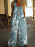 Woman wearing loose light blue floral sleeveless jumpsuit with wooden buttons and large pockets.