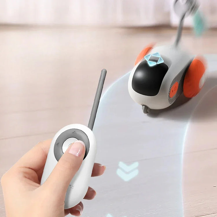 Hand using a remote control to operate a small, grey and black robot toy with orange wheels