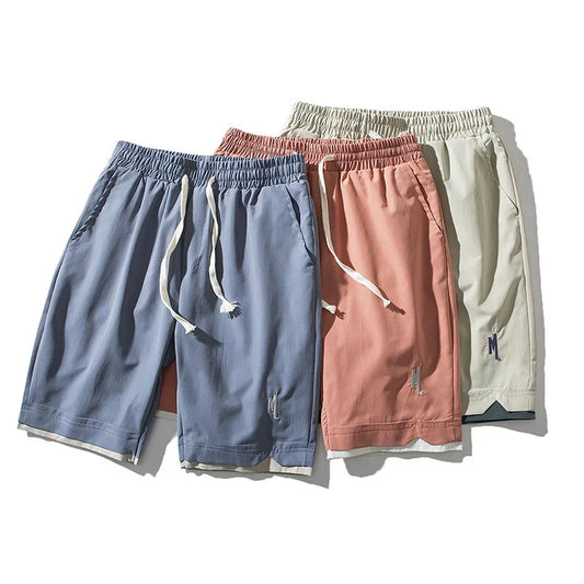 Three pairs of loose fit drawstring shorts in blue, pink, and beige with elastic waistbands.