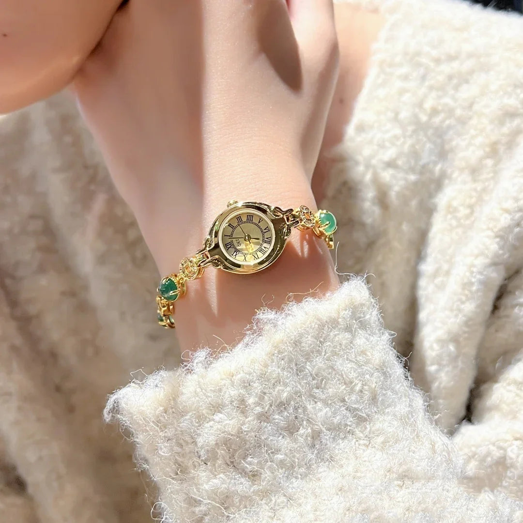 Soft textured cream sweater with a gold bracelet watch and green gemstone accents