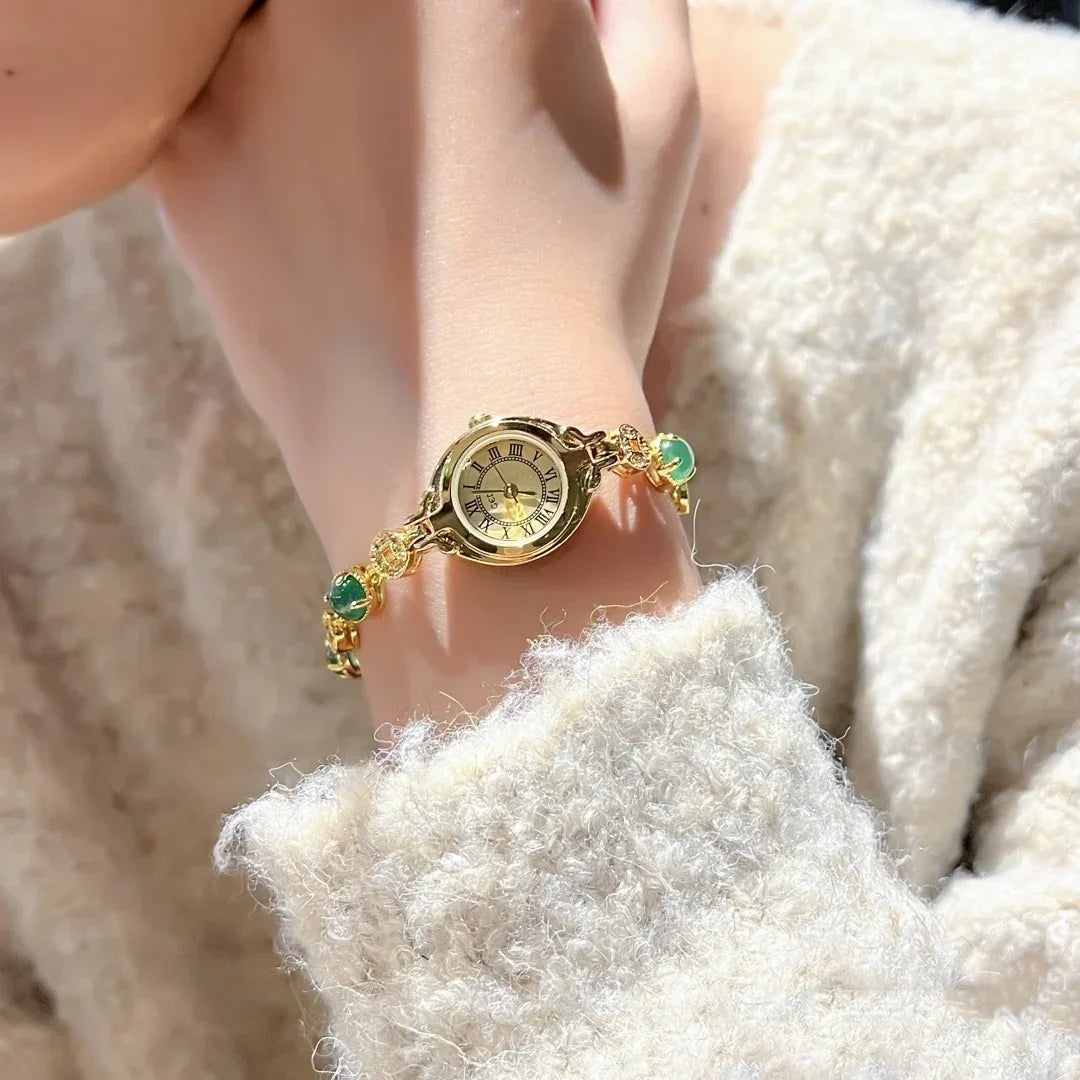 Soft textured cream sweater with a gold bracelet watch and green gemstone accents