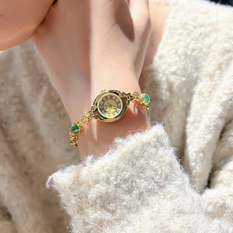 Soft textured cream sweater with a gold bracelet watch and green gemstone accents
