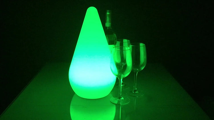 Modern green LED drop-shaped lamp with wine glasses and a wine bottle on a reflective surface