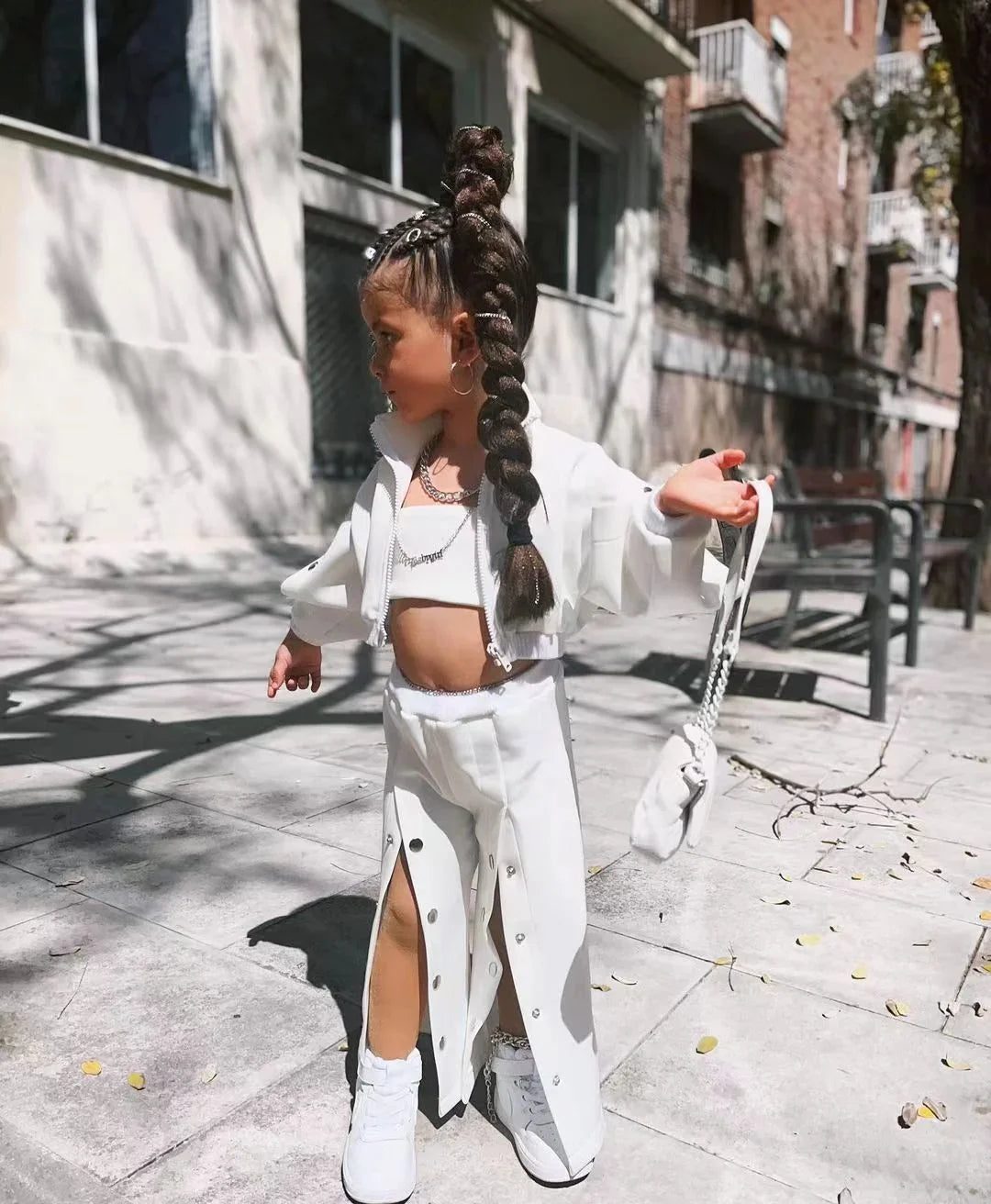 Young girl in a white streetwear set with snap-button wide leg pants, crop top, matching jacket, and sneakers