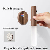 Hand holding a wooden and frosted LED wall light with built-in magnet and adhesive mount.