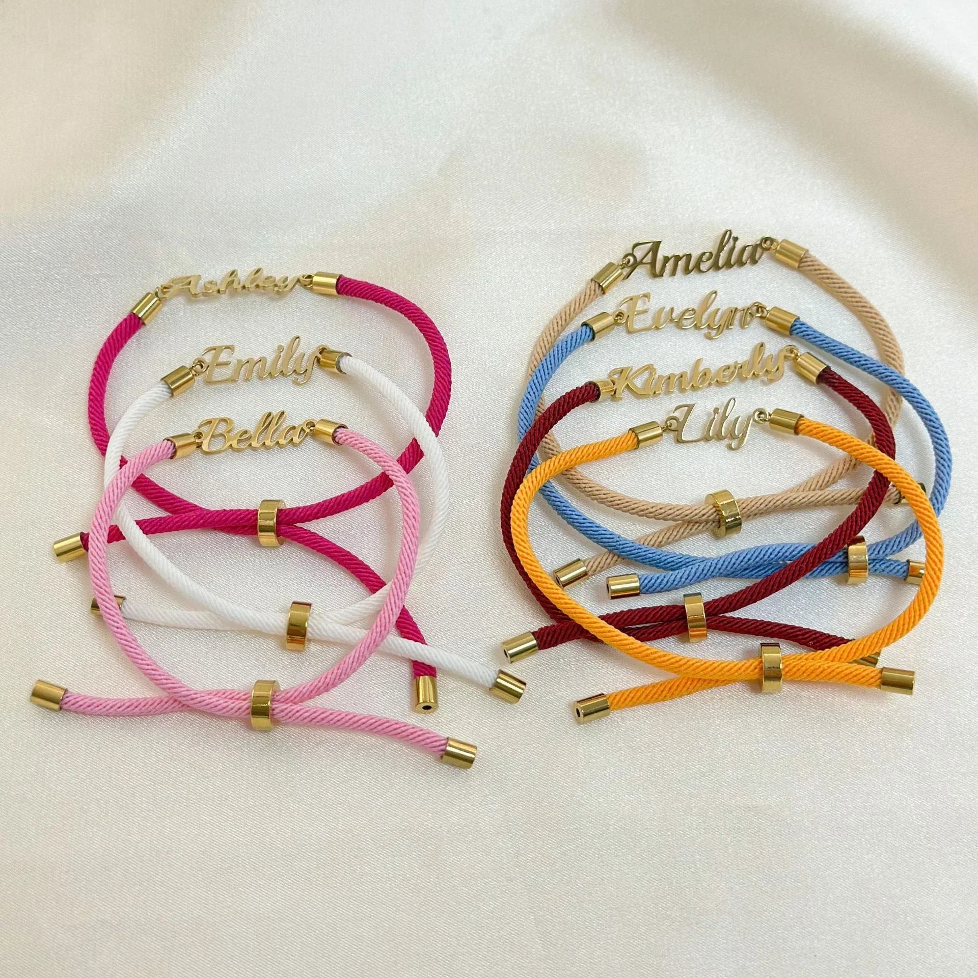 Colorful cord bracelets with gold-tone adjustable ends and nameplate charms on satin fabric