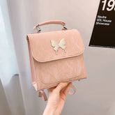 Pastel pink faux leather backpack with butterfly accent and top handle, structured fit