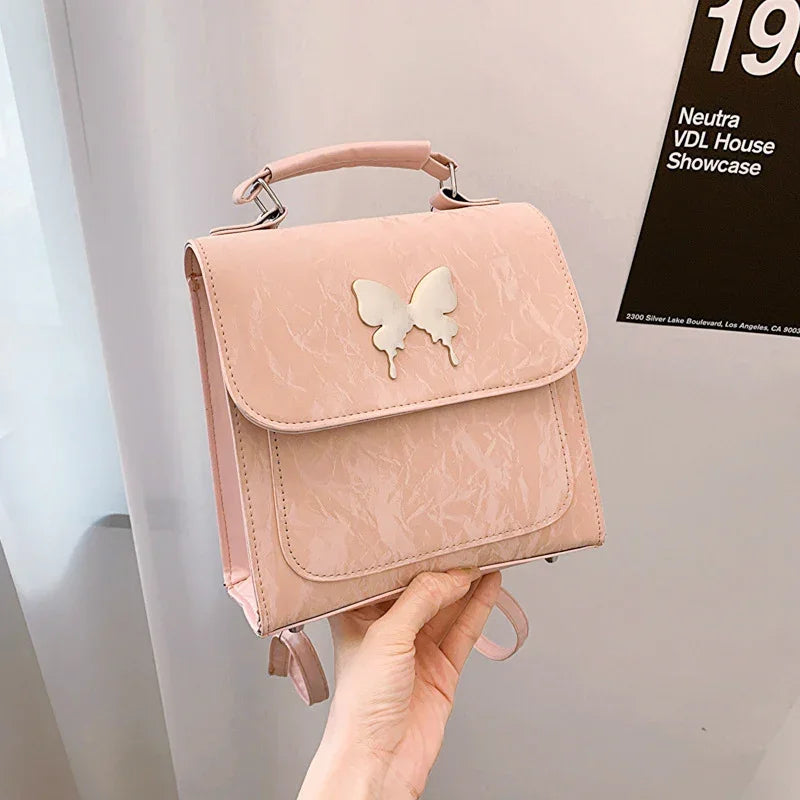 Pastel pink faux leather backpack with butterfly accent and top handle, structured fit