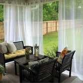 Outdoor patio with black wooden furniture, yellow and patterned cushions, sheer white curtains