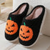 Cozy black fleece slippers with orange pumpkin face design and plush interior, slip-on style