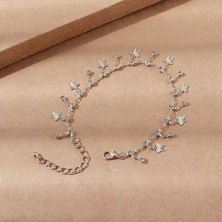 Gold chain bracelet with crystal accents and small leaf charms on beige background