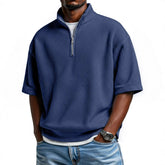 Man wearing a loose-fit blue waffle knit half-zip pullover with short sleeves and light denim jeans
