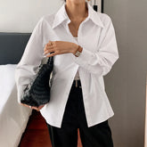 Woman wearing oversized white button-up shirt, black pants, and holding a woven black bag