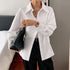 Woman wearing oversized white button-up shirt, black pants, and holding a woven black bag