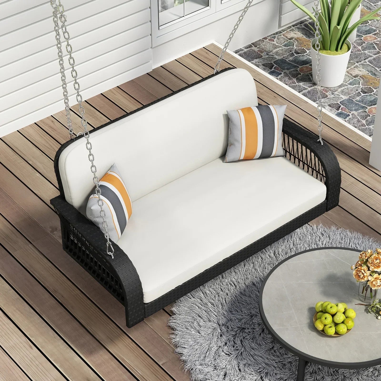 Modern black rattan porch swing with white cushions and striped accent pillows on a wooden deck