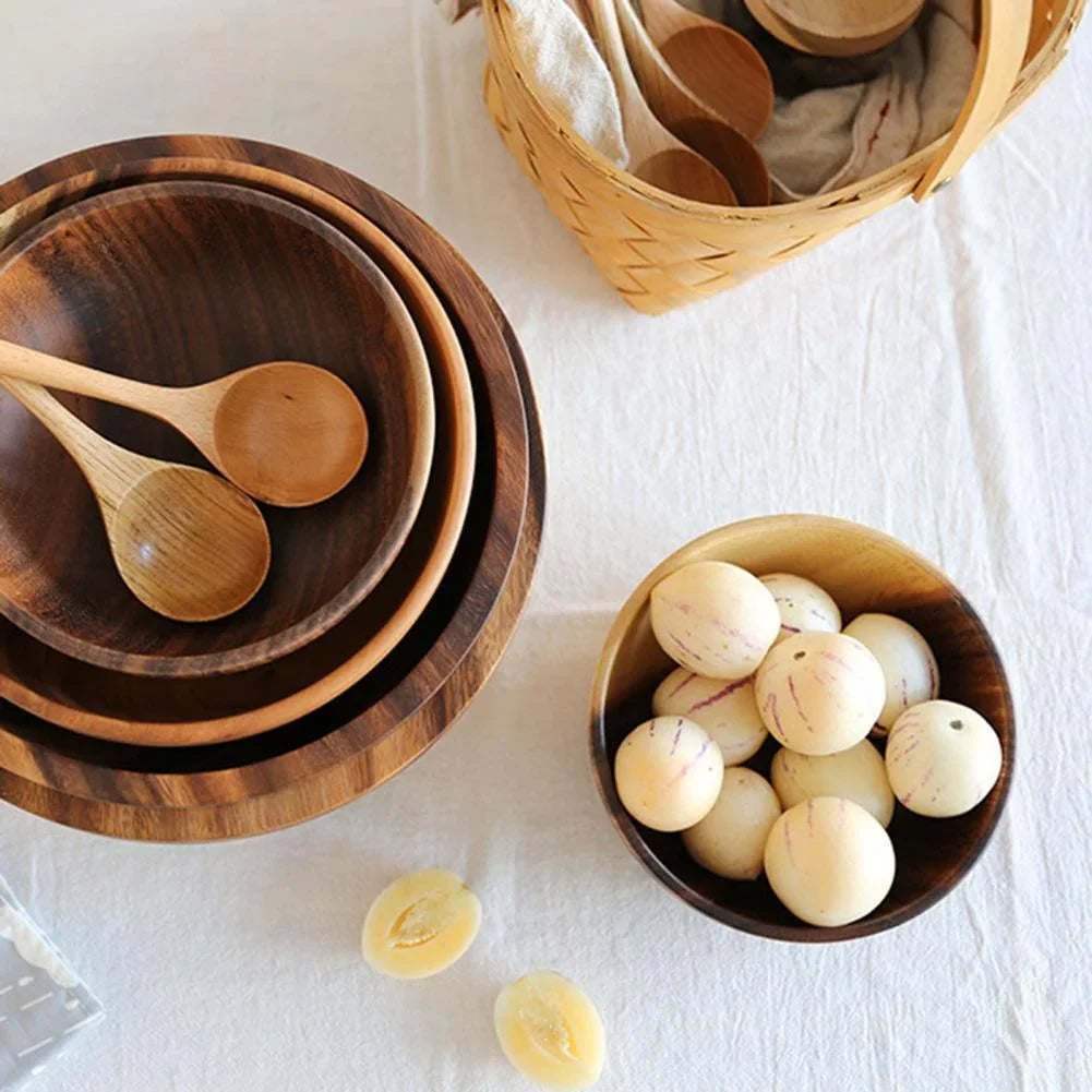 Stacked wooden bowls and spoons with fruit in a wooden bowl on a white tablecloth