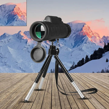Black monocular telescope with tripod, outdoor setting on wooden deck, snowy mountain background