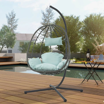 Modern egg-shaped outdoor hanging chair with light blue cushions on wooden deck by pool