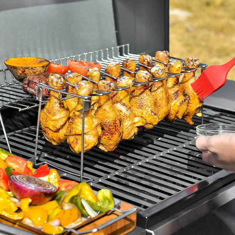 Chicken drumsticks grilling on a barbecue rack with vegetables and sauce being brushed on