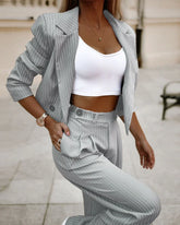 Woman wearing a gray pinstripe suit with cropped blazer and high-waisted pants, white ribbed crop top