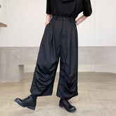 Wide-leg black pleated trousers with layered detailing, relaxed fit, styled with black shoes