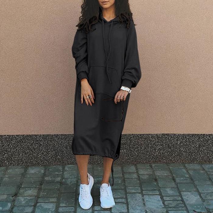 Woman wearing a loose-fit black hoodie dress with long sleeves and white sneakers, streetwear style