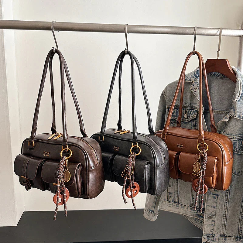 Three leather shoulder bags in brown, black, and camel with front pockets, hanging on a rack