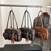 Three leather shoulder bags in brown, black, and camel with front pockets, hanging on a rack