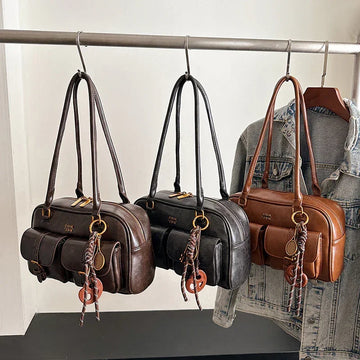 Three leather shoulder bags in brown, black, and camel with front pockets, hanging on a rack