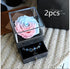 Gift box with preserved pastel pink and blue rose on top, black jewelry drawer open with beaded bracelet inside, displayed on knit fabric.