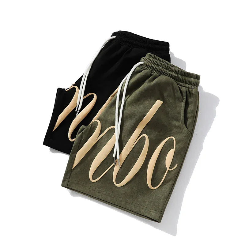 Two pairs of streetwear shorts, olive green and black, bold graphic lettering, elastic waist, drawstring, relaxed fit.