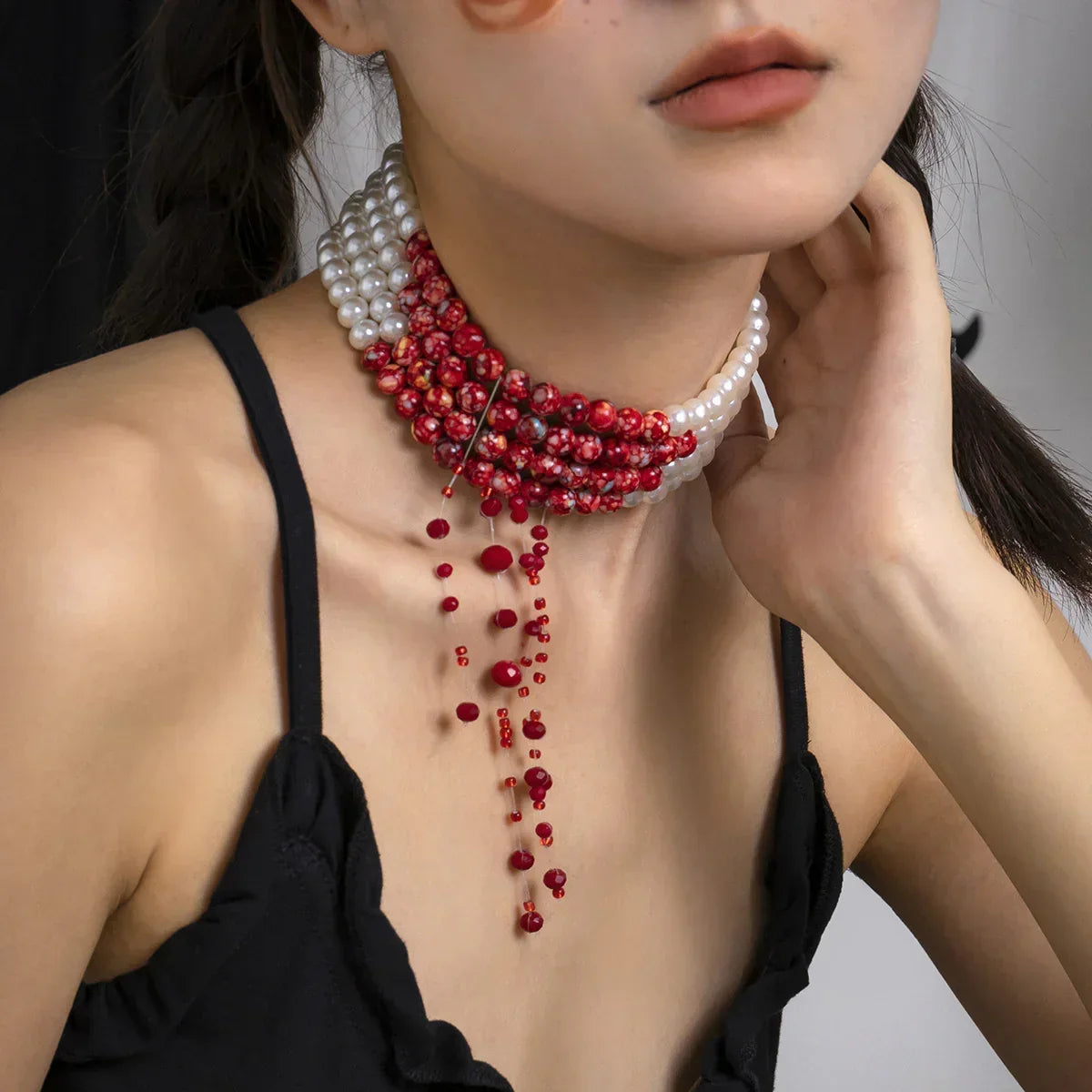 Woman wearing black spaghetti strap top with layered red and white beaded choker necklace