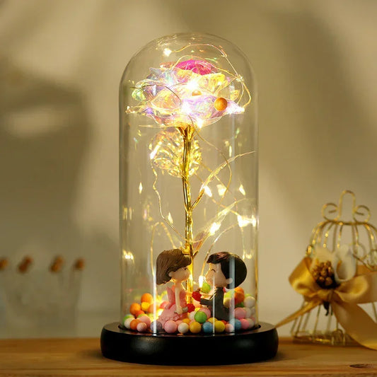 Romantic glass dome decor with LED rose flower, gold stem, and couple figurines on a wooden base