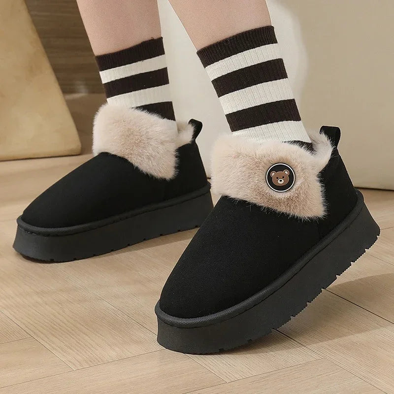 Black platform winter slippers with beige faux fur trim and bear patch, worn with striped socks