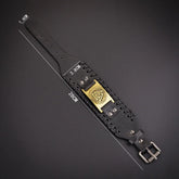 Black wide leather bracelet with metal buckle, gold emblem, and adjustable fit