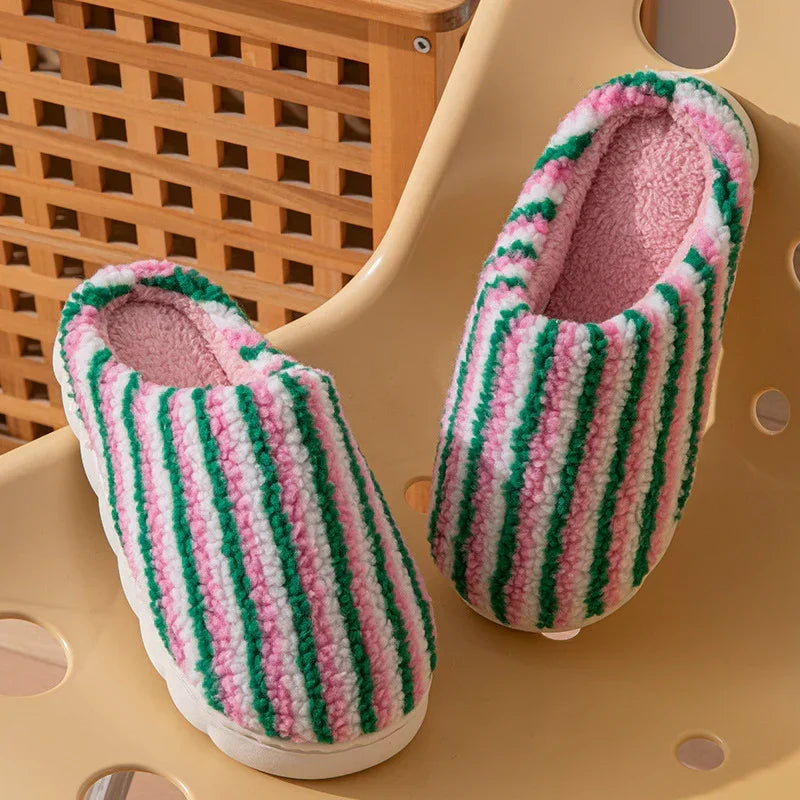 Pink and green striped fuzzy slippers with plush lining, casual fit, on a beige chair