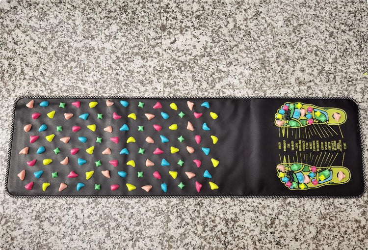 Black acupressure mat with colorful massage nodes and foot reflexology chart, laid on stone floor.