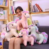 Woman in casual pastel clothing holding plush unicorn toys with rainbow manes and wings, cozy indoor setting