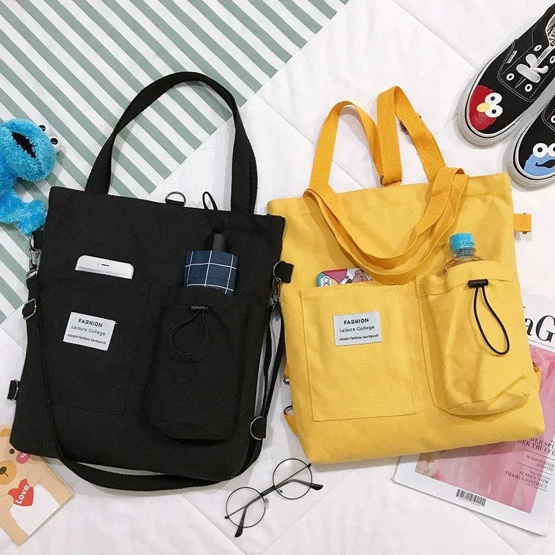 Black and yellow canvas tote bags with pockets, casual streetwear style, laid flat on bed.