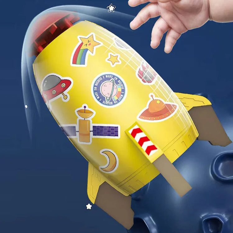 Yellow rocket-shaped toy with colorful space-themed stickers, held by a child’s hand