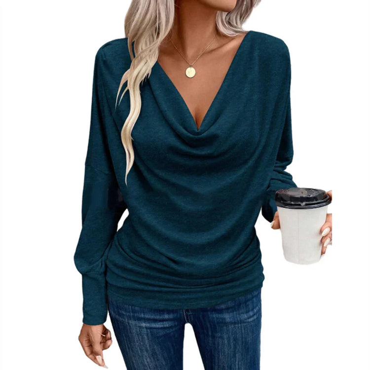 Woman wearing a teal draped cowl neck long sleeve top and fitted blue jeans