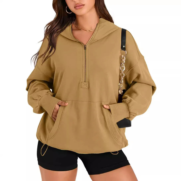 Woman wearing oversized tan quarter-zip hoodie with front pocket and black shorts, casual streetwear style